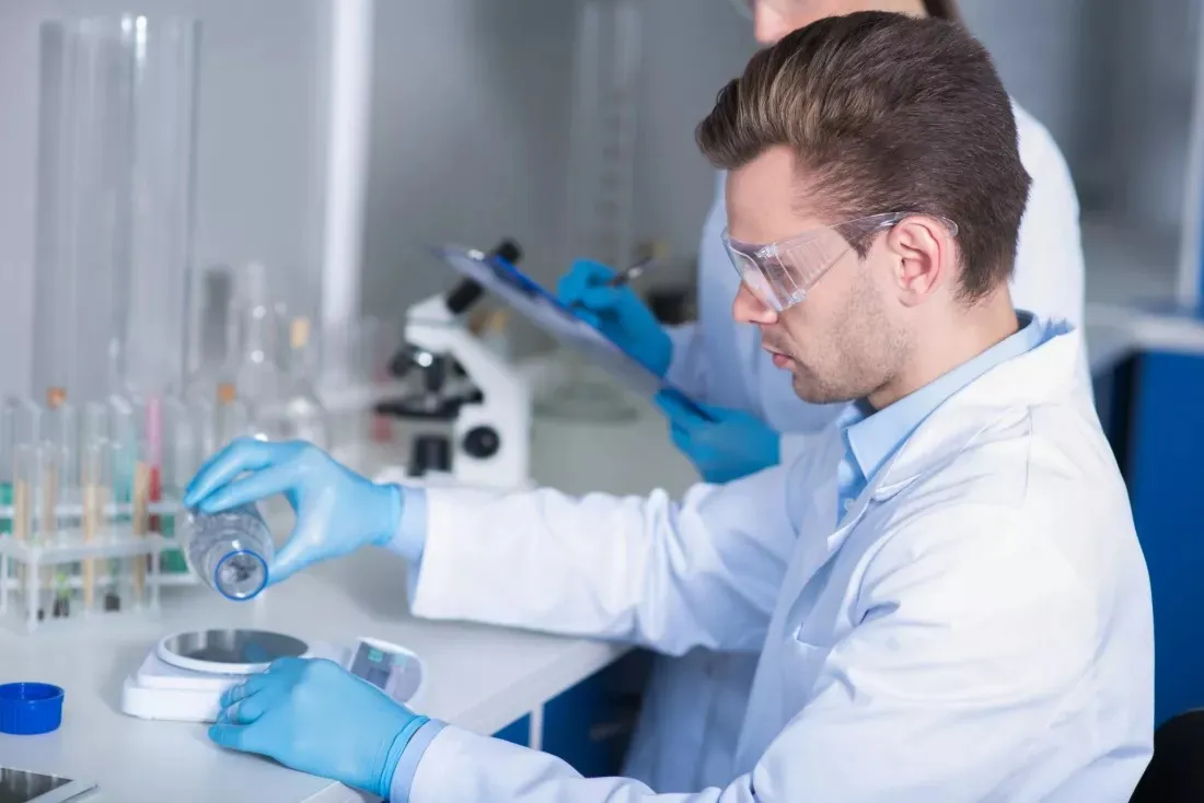 Young researcher in safety goggles weighing substances on a laboratory scale
