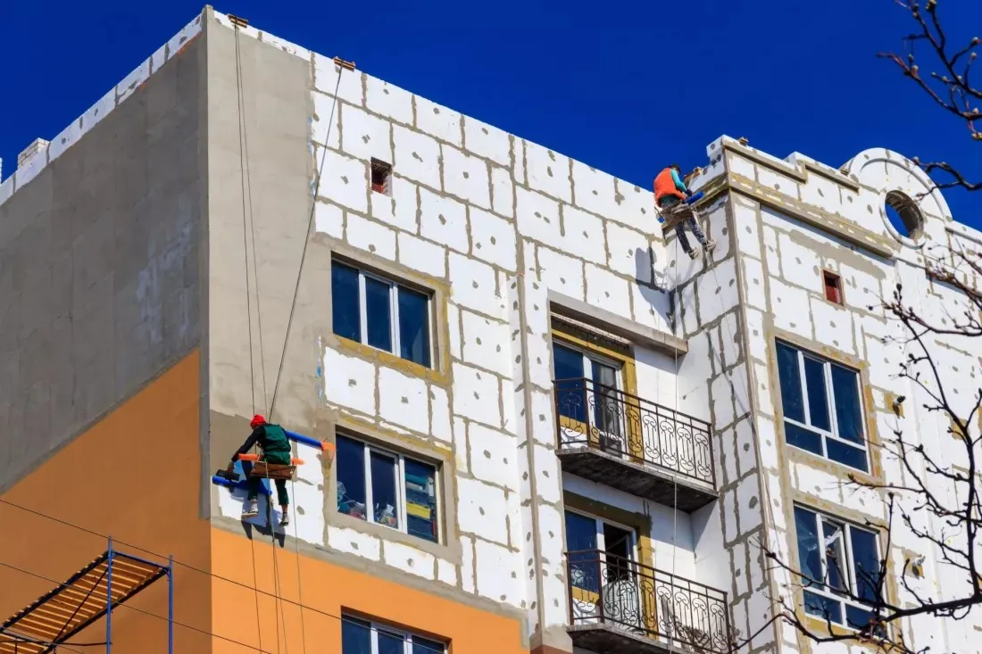 Workers insulating the facade of an older apartment block