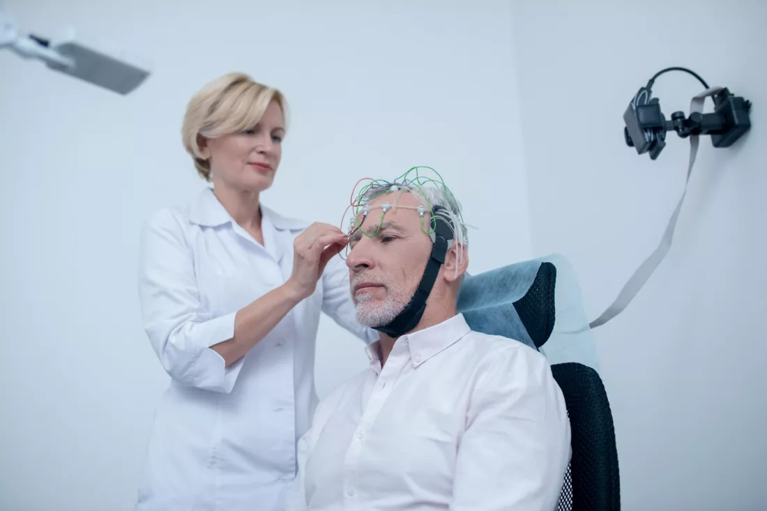 A neurologist fits an EEG electrode cap on an older patient