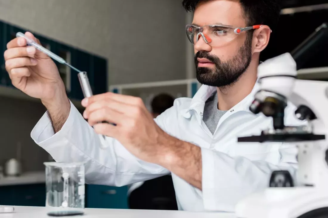 Scientist in safety glasses using a pipette to measure a sample into a test tube in a chemistry lab