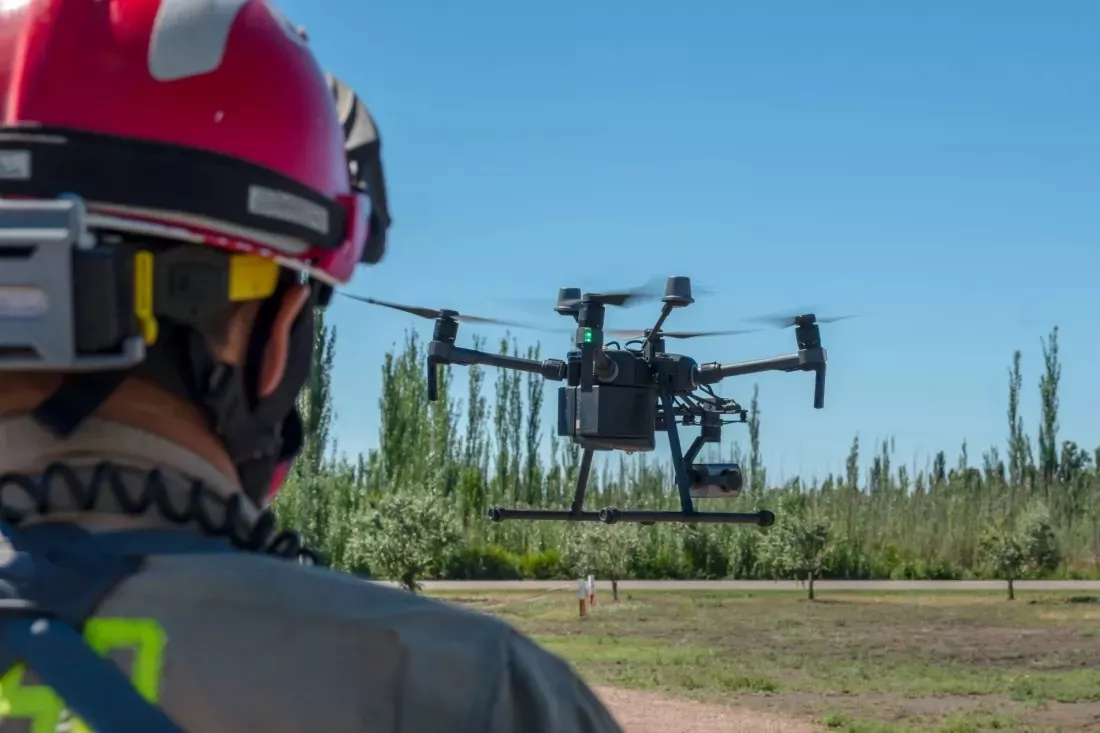 Firefighter in a helmet watching a drone flying over a field