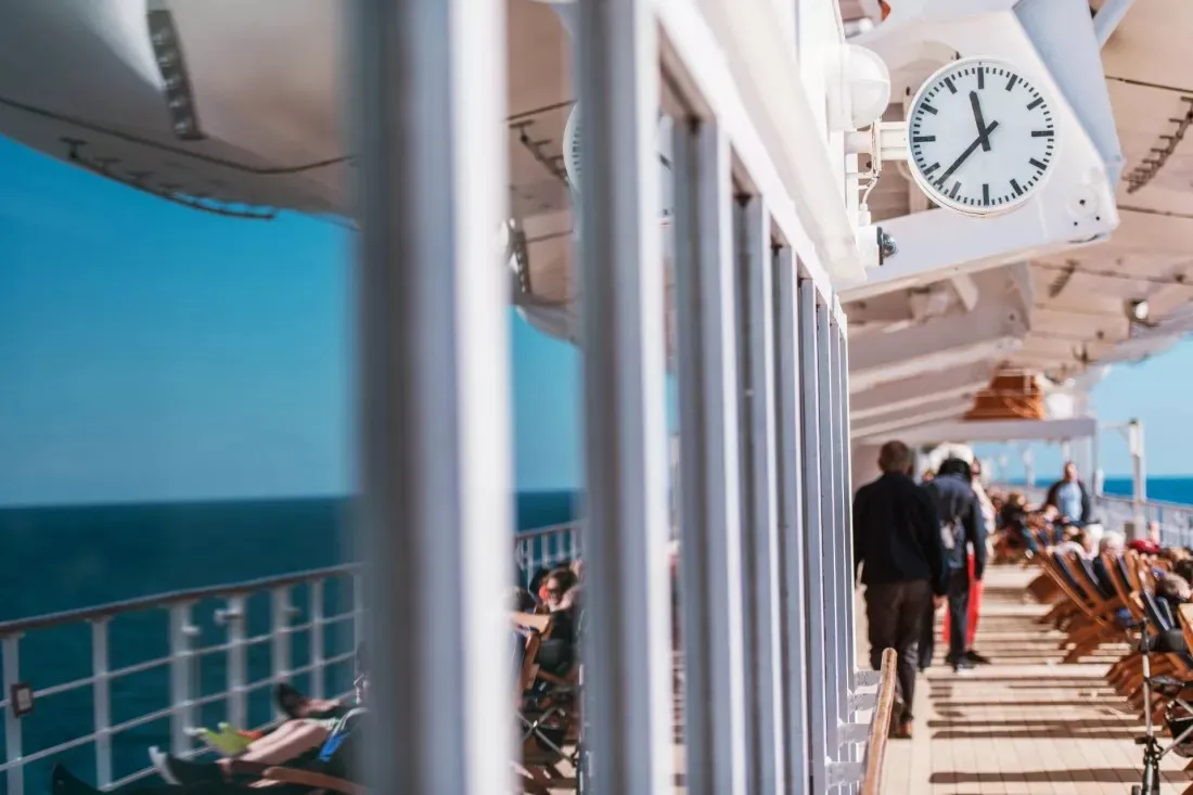 Passengers walk along the sunny deck of a cruise ship at sea